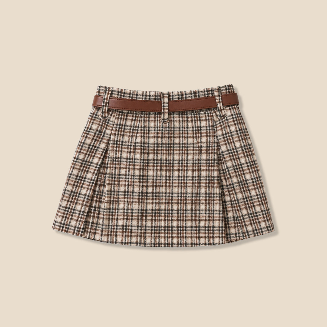 A model wearing a pleated plaid mini skirt in beige, brown, and black, paired with a white blouse and a brown belt with a gold ring, set against a solid beige background.