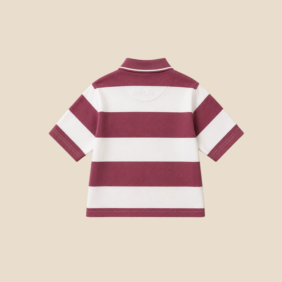 A young boy wearing a short-sleeve polo shirt with horizontal burgundy and white stripes, featuring a small white script logo on the chest, paired with khaki cargo pants, set against a solid beige background.