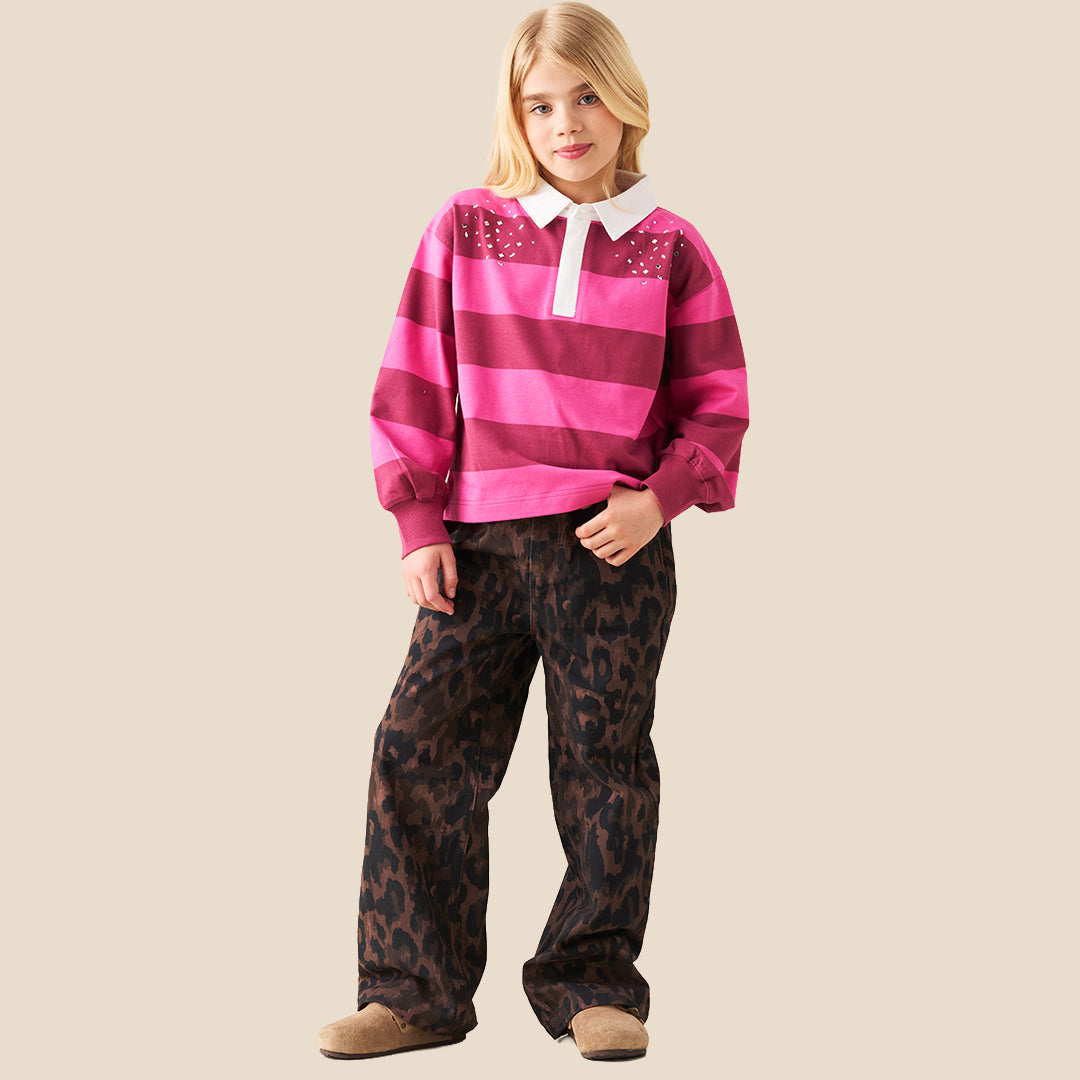 A person wearing loose, wide-leg brown and black leopard-print pants, paired with a bright pink striped long-sleeve top and tan slip-on shoes, against a plain beige background.