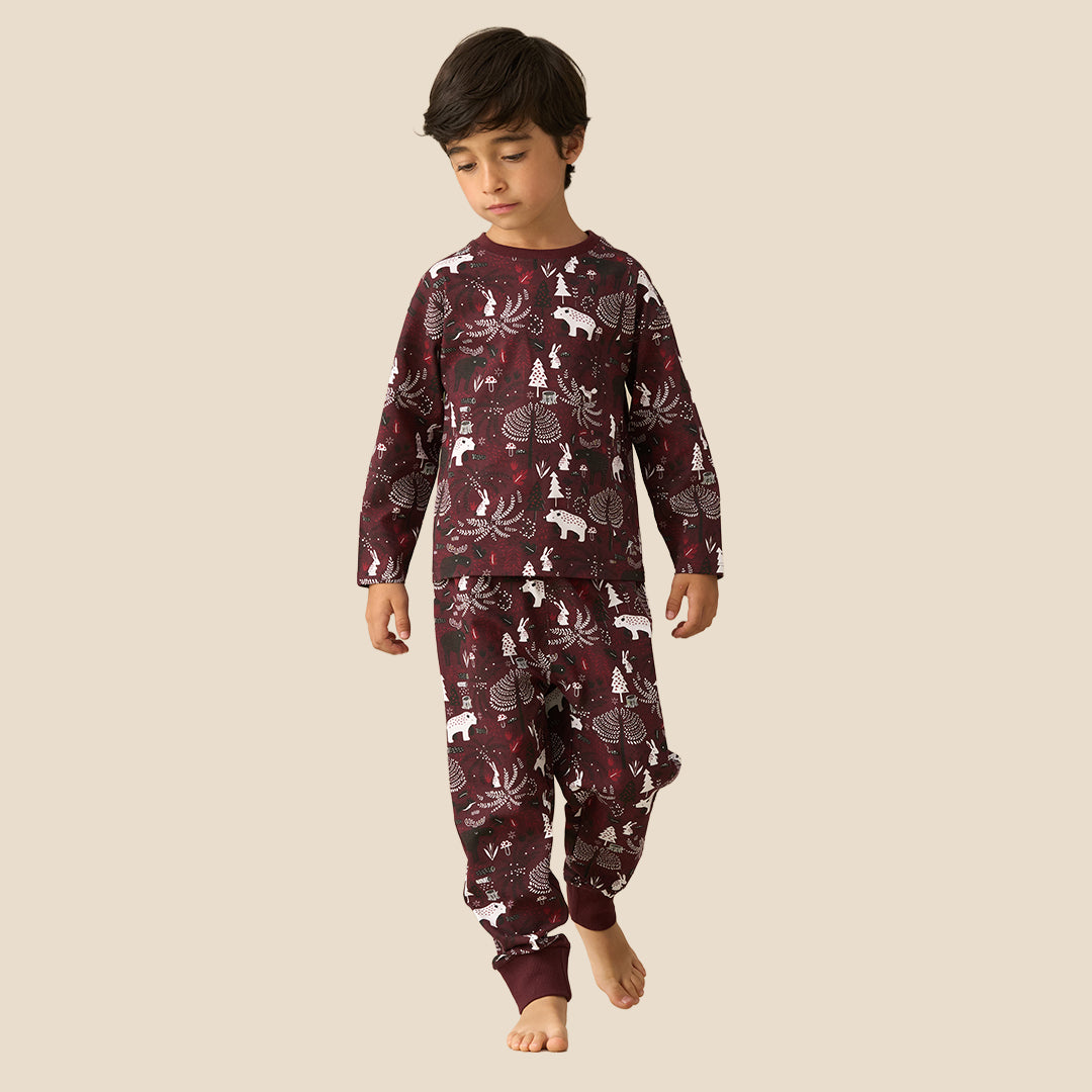 A young boy wearing a matching long-sleeve pajama set with a woodland animal print, standing against a solid light beige background.