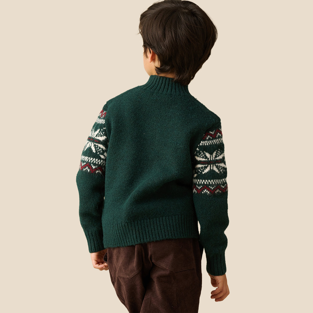 A young boy wearing a dark green knit half-zip sweater with a white and burgundy Fair Isle pattern across the chest and sleeves, paired with dark brown pants, set against a solid beige background.