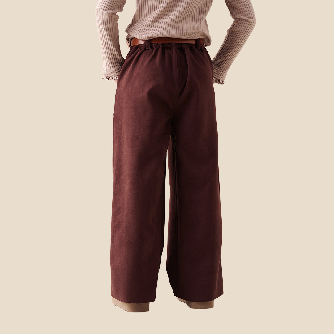 A model wearing a pair of wide-leg brown trousers with a brown belt, paired with a beige ribbed cardigan and beige slip-on shoes, set against a solid light beige background.