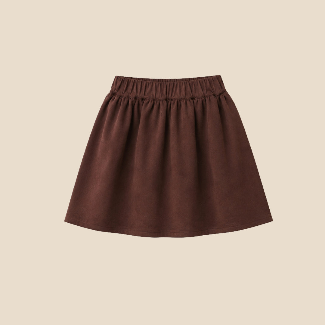 A model wearing a beige ribbed cardigan and a dark brown pleated skirt with a large bow at the waist, shown from the chest down against a solid beige background.