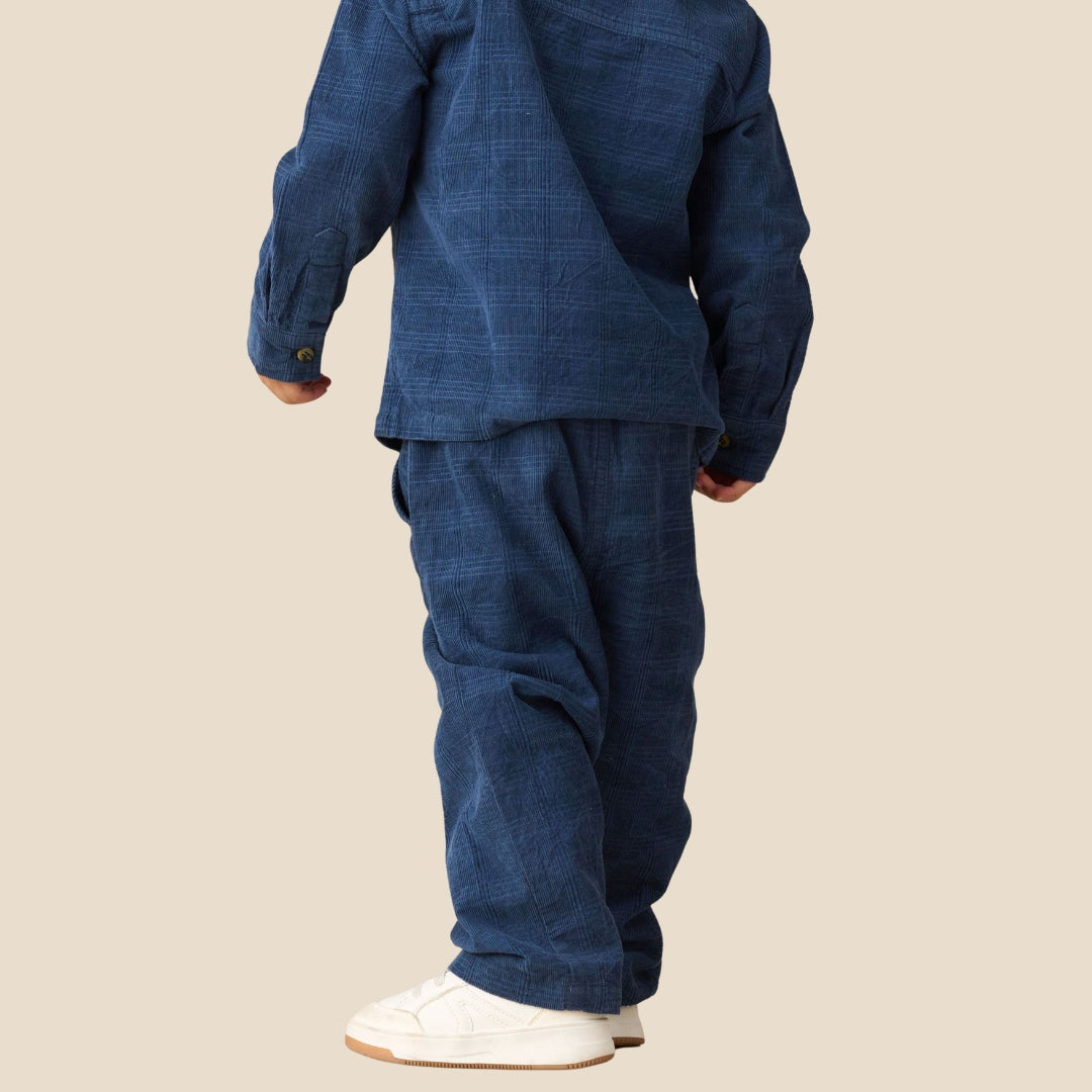 A child shown from the back wearing a matching dark blue textured two-piece outfit with white sneakers, set against a solid beige background.