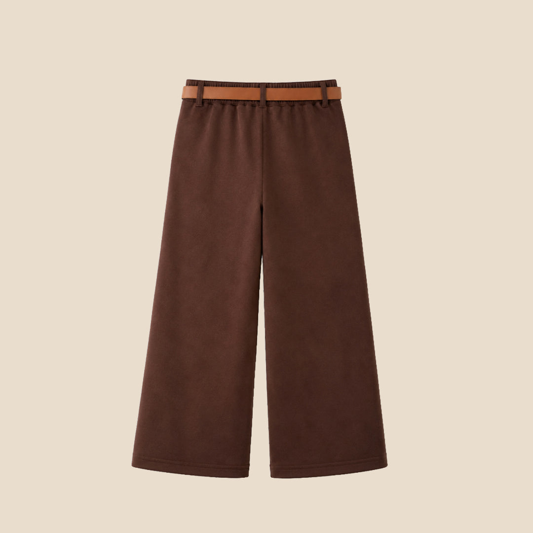 A model wearing a pair of wide-leg brown trousers with a brown belt, paired with a beige ribbed cardigan and beige slip-on shoes, set against a solid light beige background.