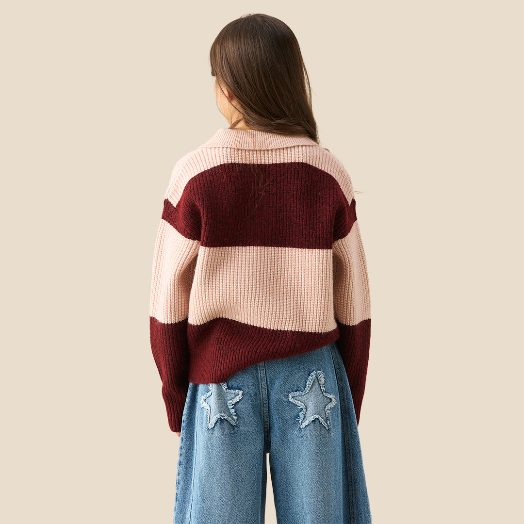 A young girl modeling a ribbed knit polo sweater with horizontal stripes in burgundy and light pink, paired with wide-leg blue jeans against a solid beige background.