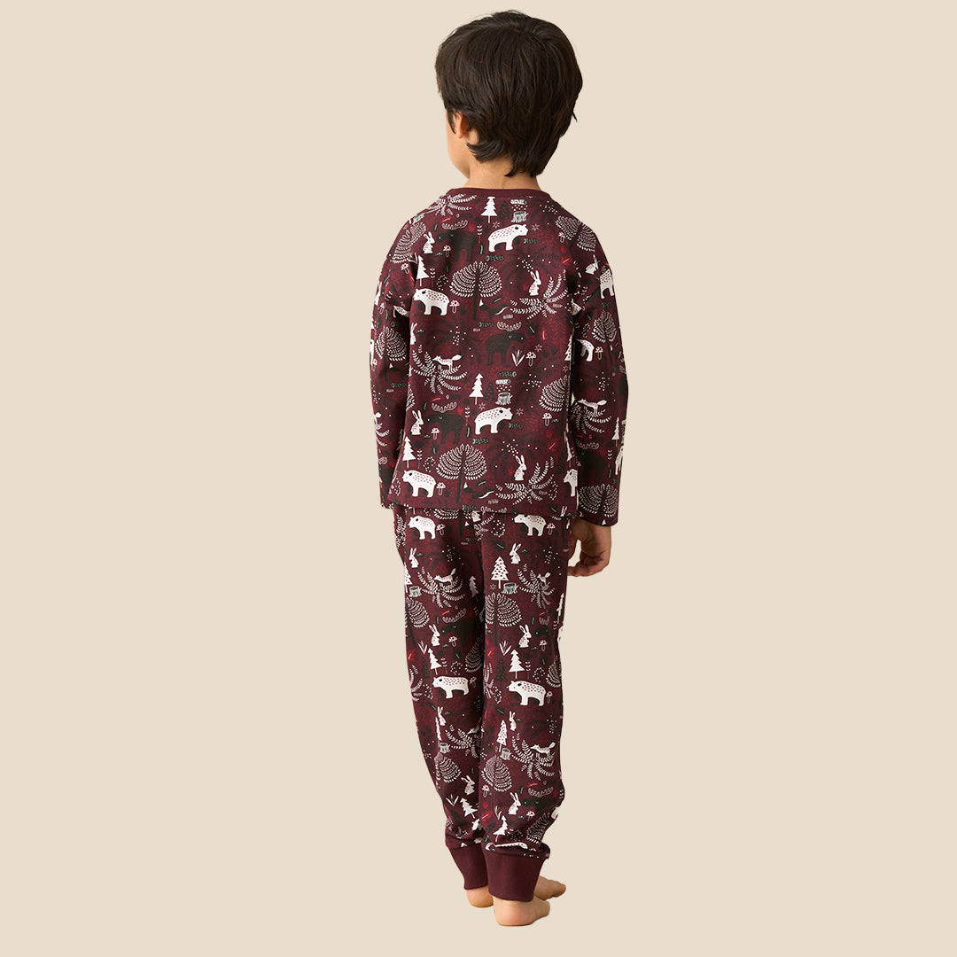 A young boy wearing a matching long-sleeve pajama set with a woodland animal print, standing against a solid light beige background.