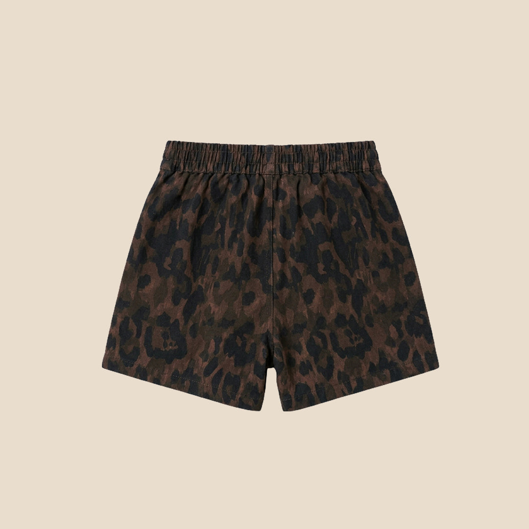 A child wearing a matching short-sleeve button-front top and shorts set in a dark brown and black leopard print, with decorative pearl-like embellishments, photographed against a plain beige background.