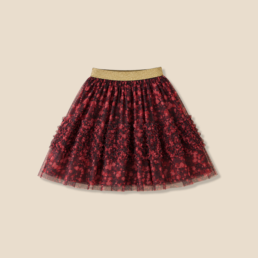 A child wearing a white long-sleeve top and a tiered tulle skirt in dark red and black floral print with a gold waistband, shown against a plain beige background.