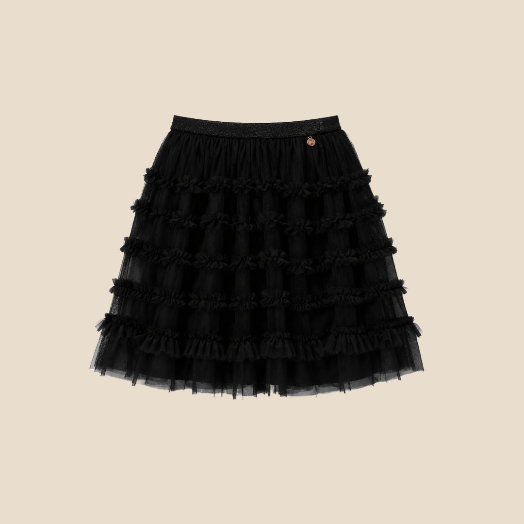 A child wearing a black puff-sleeve top with a large white bow graphic and a layered black ruffled tulle skirt, shown against a plain beige studio background.