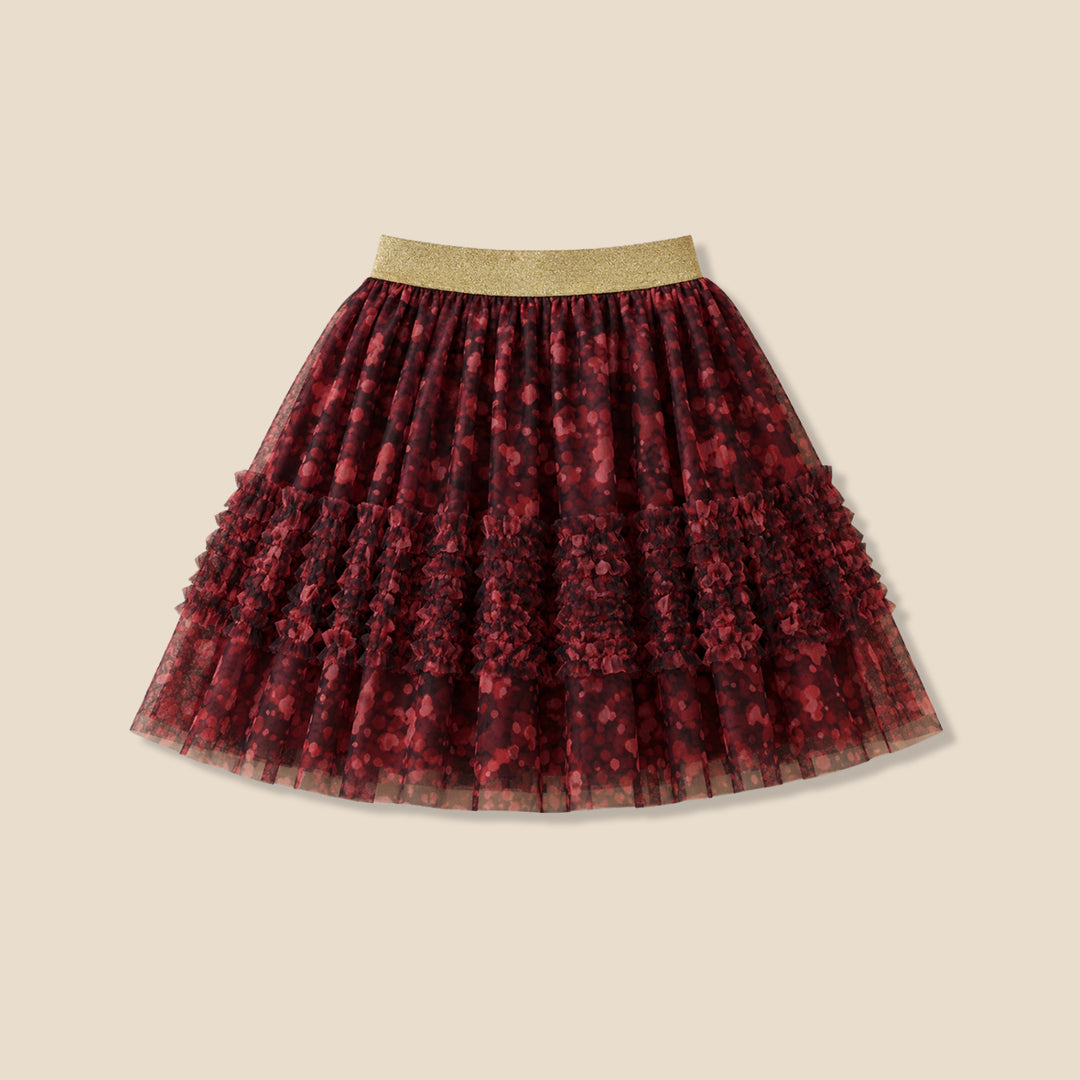 A child wearing a white long-sleeve top and a tiered tulle skirt in dark red and black floral print with a gold waistband, shown against a plain beige background.