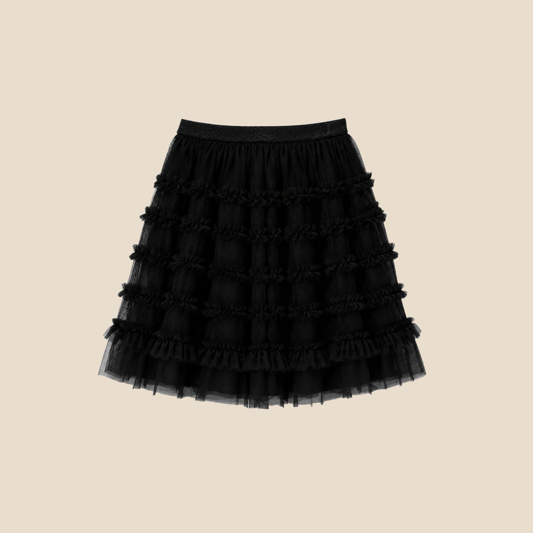 A child wearing a black puff-sleeve top with a large white bow graphic and a layered black ruffled tulle skirt, shown against a plain beige studio background.