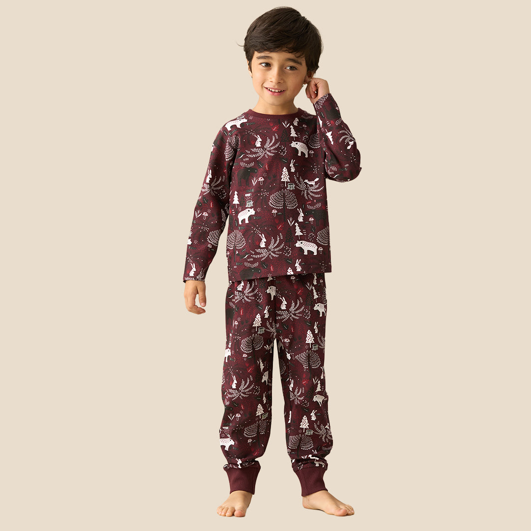 A young boy wearing a matching long-sleeve pajama set with a woodland animal print, standing against a solid light beige background.