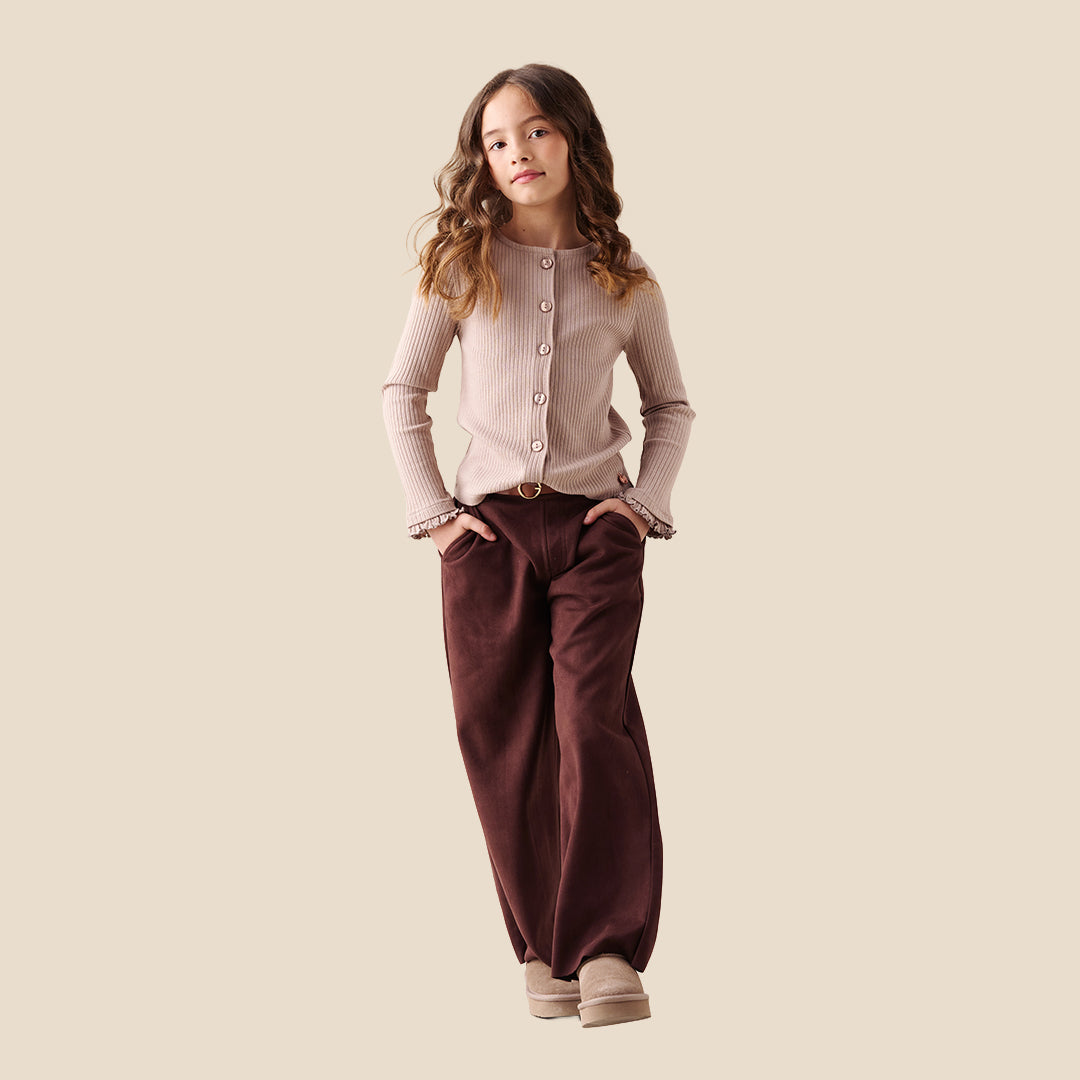 A model wearing a pair of wide-leg brown trousers with a brown belt, paired with a beige ribbed cardigan and beige slip-on shoes, set against a solid light beige background.