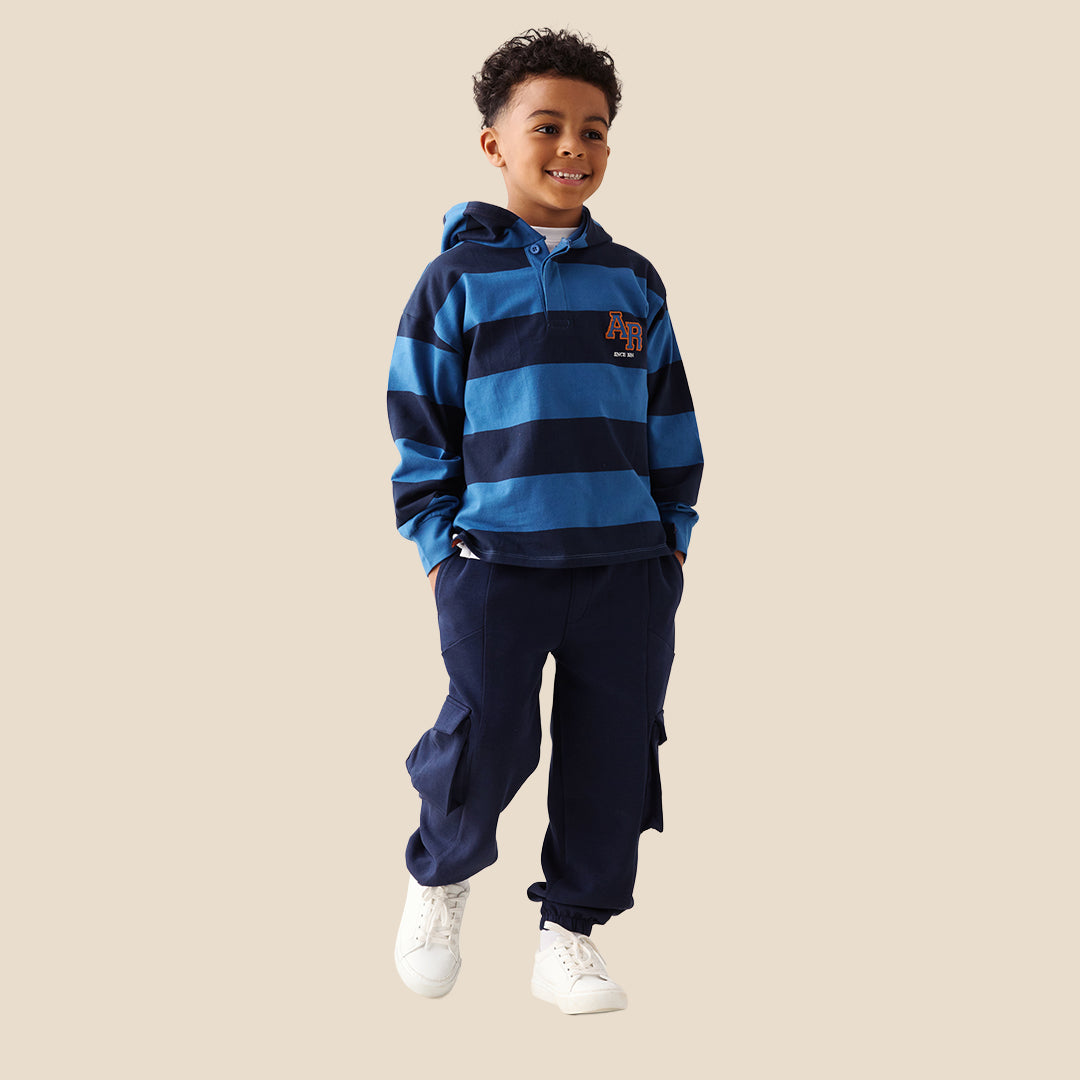A child wearing navy blue cargo pants with side flap pockets, a blue and navy striped long-sleeve shirt, and white sneakers, standing against a solid beige background.